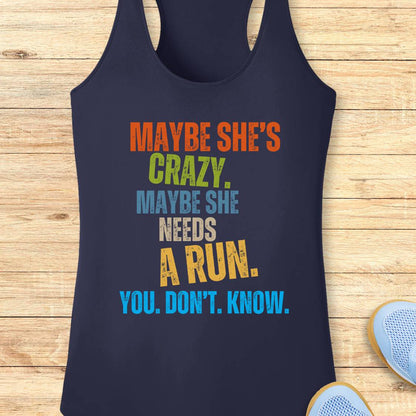 A navy blue performance racerback tank top with a colorful motivational text graphic reading 'MAYBE SHE'S CRAZY. MAYBE SHE NEEDS A RUN.