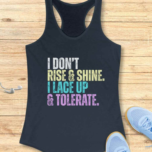 Dark navy racerback tank top with the phrase I DON'T RISE & SHINE I LACE UP & TOLERATE in white yellow light blue and purple text placed on a rustic wooden surface next to light blue athletic shoes and white earbuds
