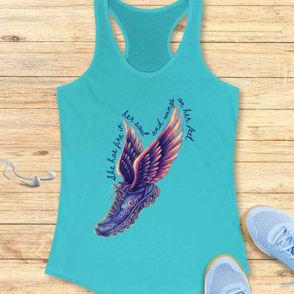 Turquoise blue racerback tank top with a vibrant winged running shoe graphic in purple orange and pink, featuring the quote "she has fire in her soul and wings on her feet" displayed on a light wooden background with accompanying light blue running shoes and white earphones