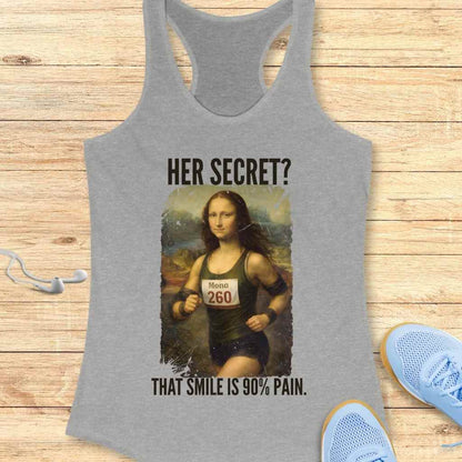 Digital print on a gray tank top featuring a parody of Leonardo da Vinci's Mona Lisa depicted as a runner in her iconic sfumato landscape, wearing a green singlet with a "Mona 260" bib, humorously captioned "HER SECRET? THAT SMILE IS 90% PAIN" and displayed on a wooden surface with white earbuds and light blue running shoes