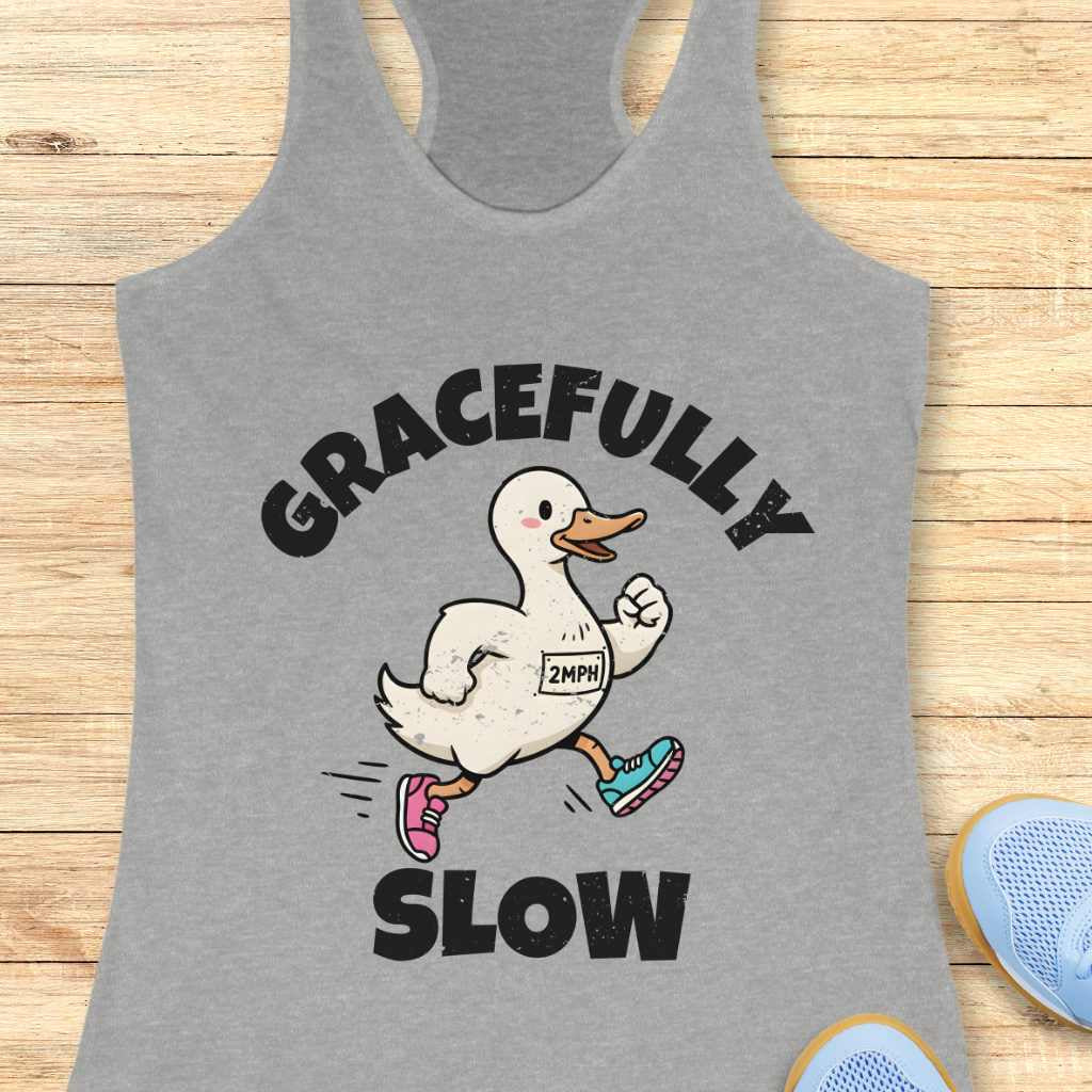 Gray tank top with a cartoon duck and text 'gracefully slow' ,on a wooden surface
