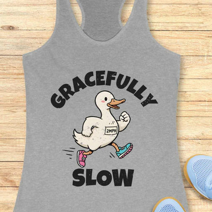 Gray tank top with a cartoon duck and text 'gracefully slow' ,on a wooden surface
