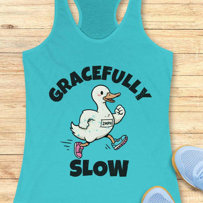Turquoise tank top with a cartoon duck and text 'gracefully slow' , on a wooden surface