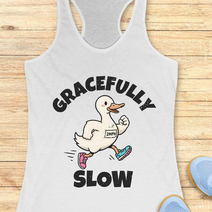 Gray tank top with a cartoon duck and text 'GRACEFULLY SLOW' on a wooden surface.