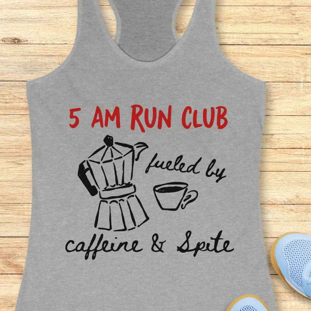 Gray racerback tank top featuring a red "5 AM RUN CLUB" slogan above a black line drawing of a moka pot and coffee cup, with "fueled by caffeine & Spite" in black script, displayed on a light wooden background with a light blue running shoe partially visible