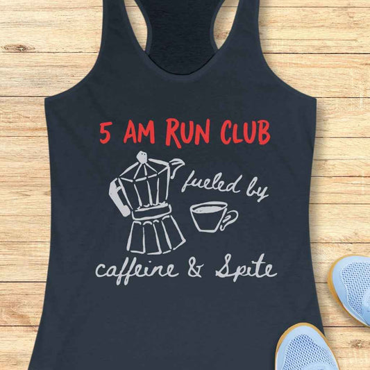 Printed navy blue racerback tank top on a light wooden surface features red text 5 AM RUN CLUB, a white Moka pot with coffee cup, and fueled by caffeine & Spite in white script, with light blue running shoes visible nearby