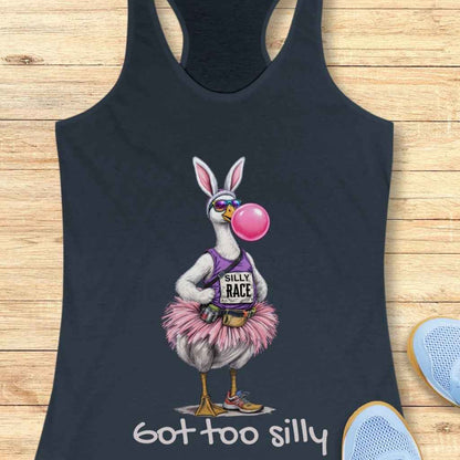 Illustration of a whimsical goose on a dark blue tank top wearing a bunny ears headband, sunglasses, a purple 'Silly Race' tank top, a pink tutu, a fanny pack, running shoes, blowing a large pink bubblegum bubble, with the text 'got too silly' below on a wooden background