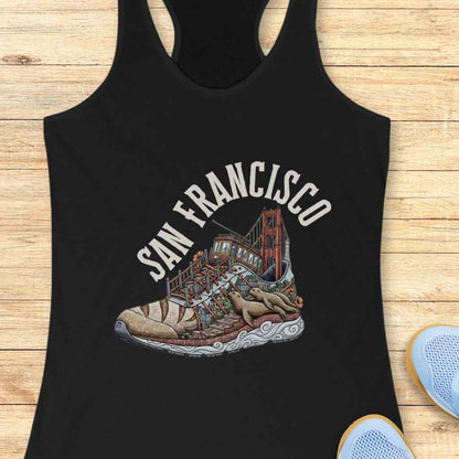 Graphic design on a black tank top depicting a vibrant San Francisco cityscape ingeniously shaped as a sneaker, featuring the iconic Golden Gate Bridge as the heel, a colorful cable car on a winding street, and two brown sea lions lounging on the patterned sole, beneath arched SAN FRANCISCO text
