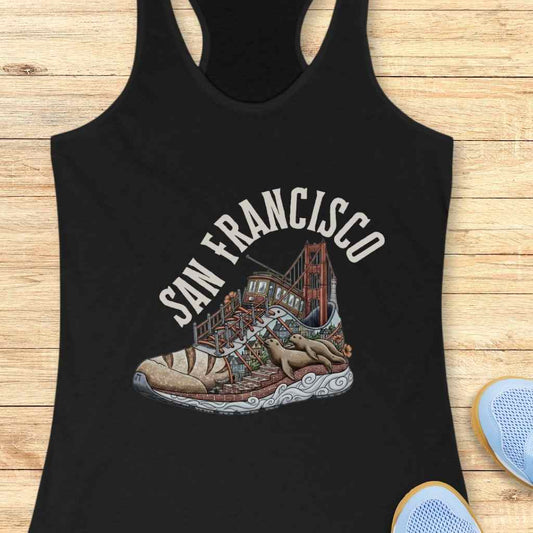 Graphic design on a black tank top depicting a vibrant San Francisco cityscape ingeniously shaped as a sneaker, featuring the iconic Golden Gate Bridge as the heel, a colorful cable car on a winding street, and two brown sea lions lounging on the patterned sole, beneath arched SAN FRANCISCO text