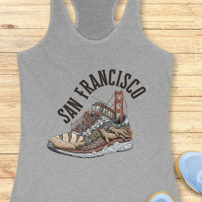 Screen-printed graphic on a grey tank top showcasing a stylized running shoe filled with a vibrant San Francisco cityscape featuring the Golden Gate Bridge, a classic cable car, brick streets, and two lounging sea lions, all beneath the arched text SAN FRANCISCO