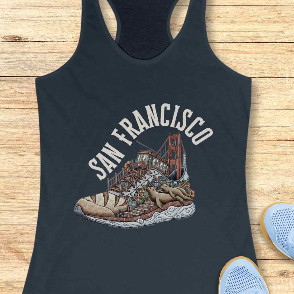 Graphic print on a navy tank top depicting San Francisco landmarks inside a running shoe with the Golden Gate Bridge, a cable car, colorful houses on brick steps, and two sea lions lounging on a wavy white sole below the text San Francisco