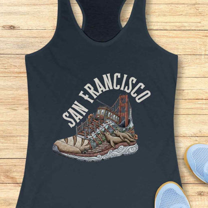 Graphic print on a navy tank top depicting San Francisco landmarks inside a running shoe with the Golden Gate Bridge, a cable car, colorful houses on brick steps, and two sea lions lounging on a wavy white sole below the text San Francisco