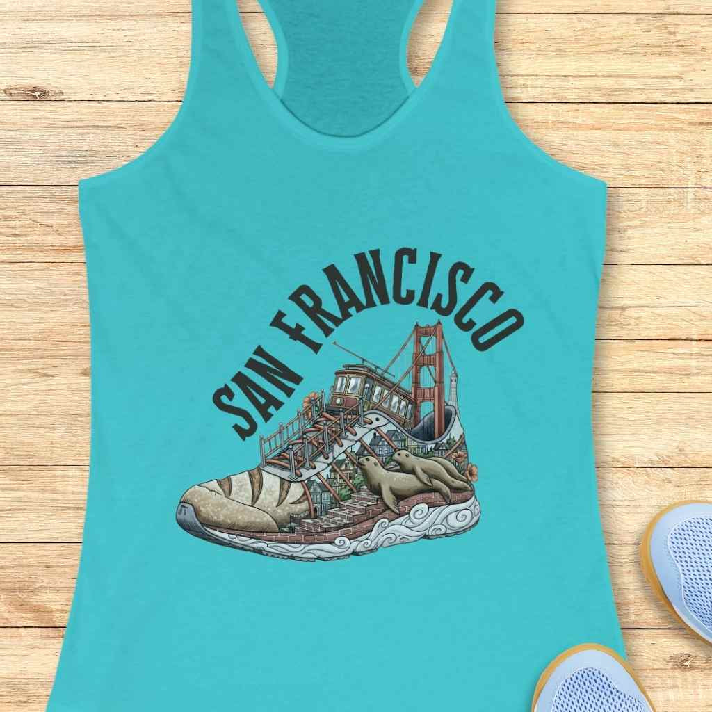 Graphic print on a teal tank top depicting a San Francisco cityscape within a running shoe, showcasing the Golden Gate Bridge, a cable car, Lombard Street-like steps, and two lounging sea lions on the sole, with 'SAN FRANCISCO' text arching above