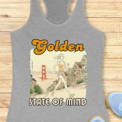 Graphic print on a grey tank top showing a woman in a yellow tank top and grey shorts jogging up a San Francisco street with the red Golden Gate Bridge and colorful Victorian Painted Ladies houses in the background, featuring "Golden" in yellow script and "STATE OF MIND"