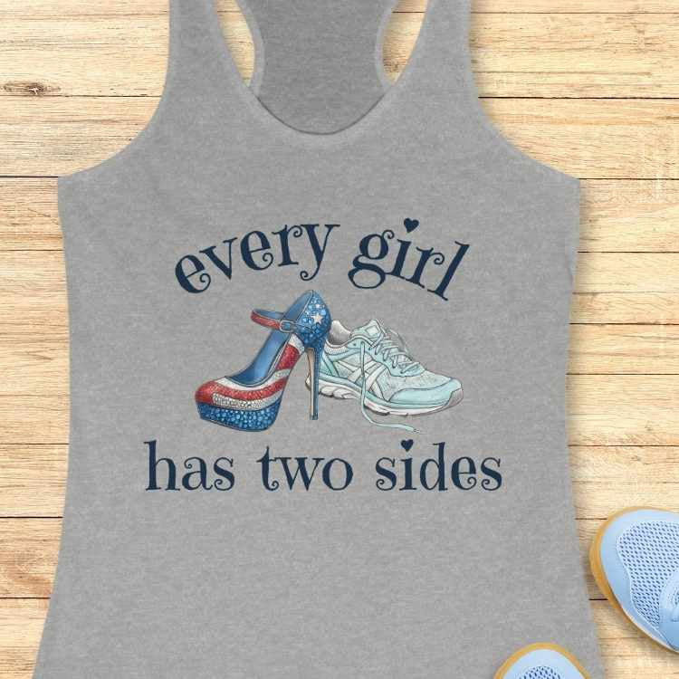 Gray tank top with high-heeled shoe and sneakers design and text 'every girl has two sides' on a wooden surface.