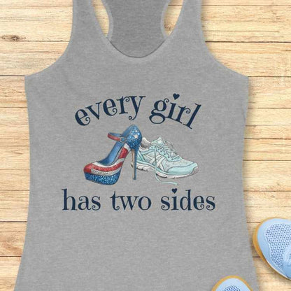 Gray tank top with high-heeled shoe and sneakers design and text 'every girl has two sides' on a wooden surface.