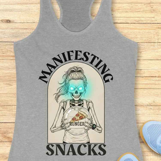 Gray tank top with a graphic design of a skeleton holding pizza and text 'Manifesting Hunger Snacks' on a wooden surface.