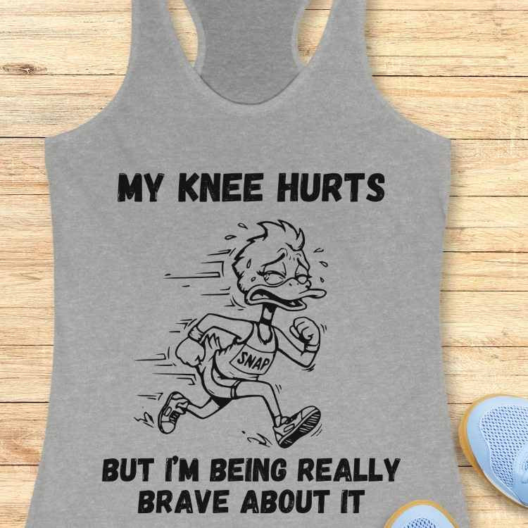 Graphic design on a grey tank top featuring a cartoon duck crying and sweating in a 'SNAP' bib while running, with the text MY KNEE HURTS BUT I'M BEING REALLY BRAVE ABOUT IT