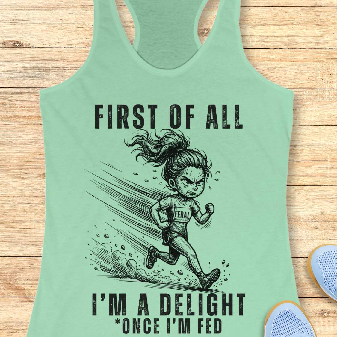 Mint green tank top with a graphic of a running girl and text first  of all I'm a delight , once I'm fed, on a wooden surface
