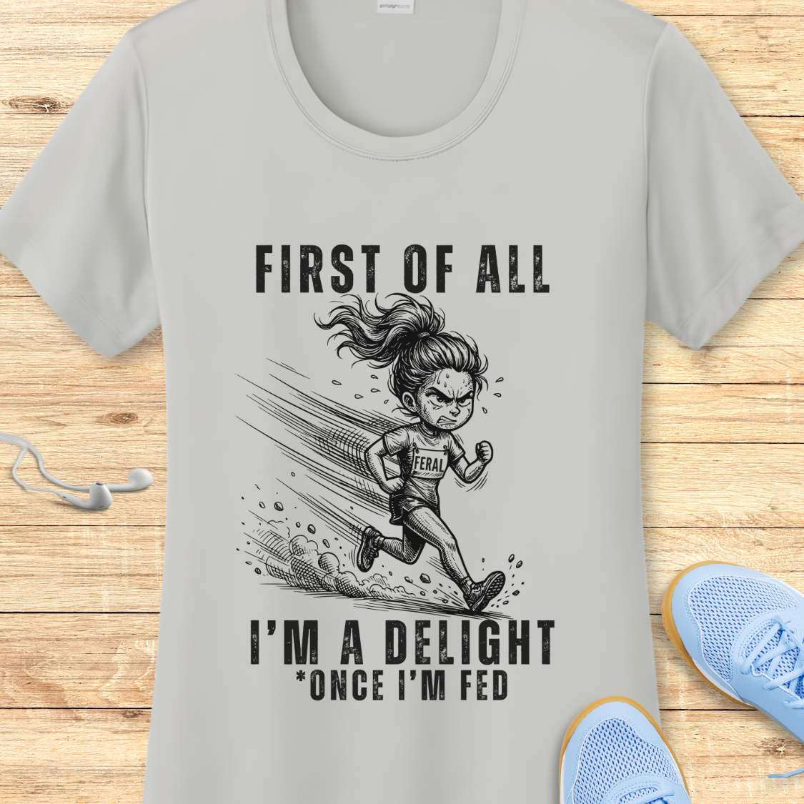silver performance tee with a graphic of a running girl and text first  of all I'm a delight , once I'm fed, on a wooden surface