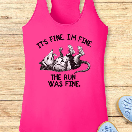 A bright pink performance racerback tank top laid flat on a light wood surface, featuring a black graphic of a running mouse and the text 'IT'S FINE. I'M FINE.