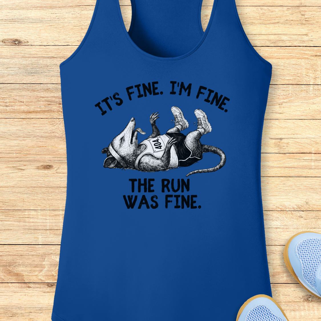 A royal blue racerback performance tank top laid flat on a light wood background, featuring a humorous graphic of a running mouse lying on its back with the text 'IT'S FINE. I'M FINE.