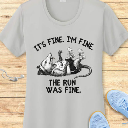 silver performance t-shirt with possum image and text 'It's fine. I'm fine. The run was fine.'  on a wooden surface with sneakers.