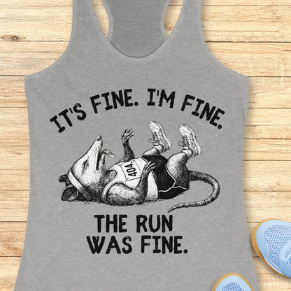 Gray tank top with possum
 graphic and text on a wooden surface