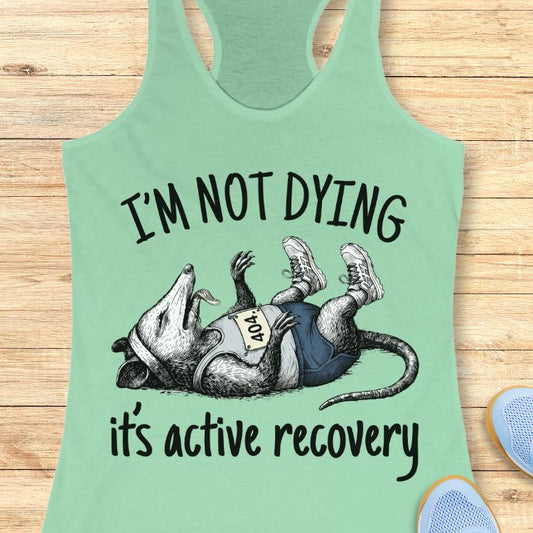 Light green tank top with possum graphic and text on a wooden surface
