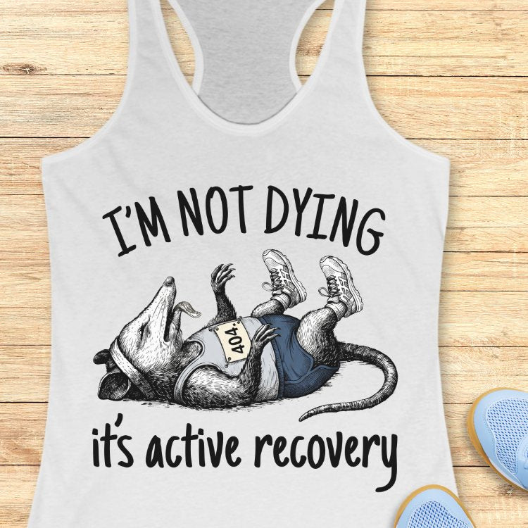 Gray tank top with a graphic of a rat and text 'I'm not dying, it's active recovery' on a wooden surface.