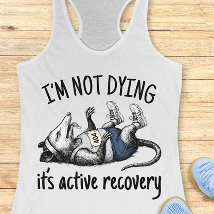 Gray tank top with a graphic of a rat and text 'I'm not dying, it's active recovery' on a wooden surface.