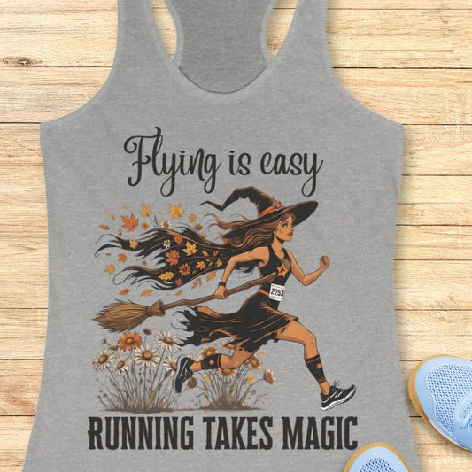 Gray tank top with a witch running on a broom design and text 'Flying is easy, running takes magic' on a wooden surface.