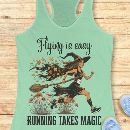 Mint green tank top with a witch graphic and text 'Flying is easy, running takes magic' on a wooden surface