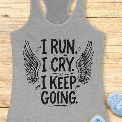 Gray tank top with motivational quote  "I run. I cry. I keep going." and wings on a wooden surface