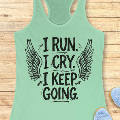 Mint green tank top with motivational text  "I run. I cry. I keep going." and wings on a wooden surface