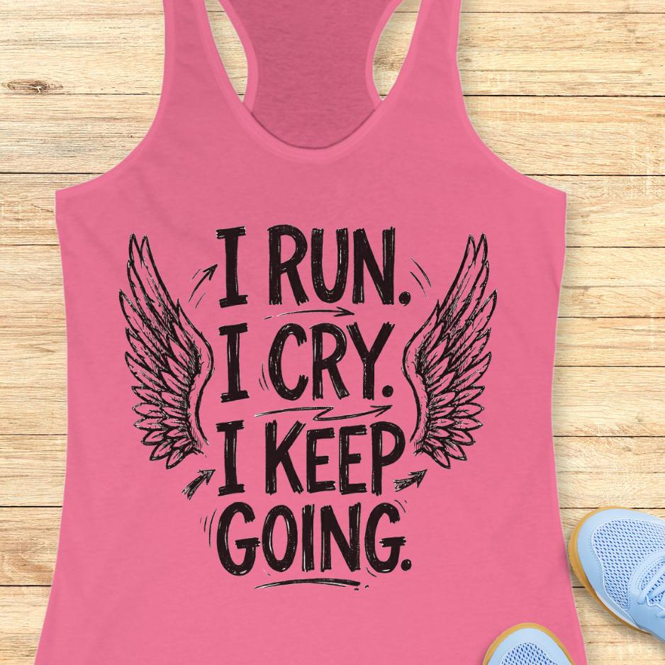 Pink tank top with motivational text  "I run. I cry. I keep going." and wings on a wooden surface