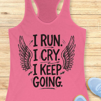 Pink tank top with motivational text  "I run. I cry. I keep going." and wings on a wooden surface