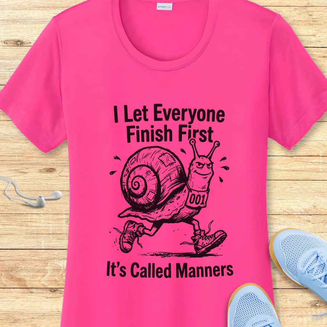 Pink t-shirt with a snail graphic and text on a wooden surface
