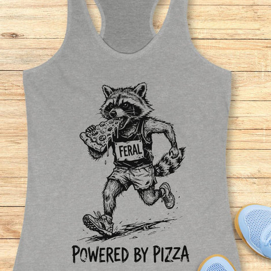 grey tank top with a raccoon runner, with a bib that says - feral, and it is eating a slice of pizza. The tank top has the text  -powered by pizza, and it's on a wooden background