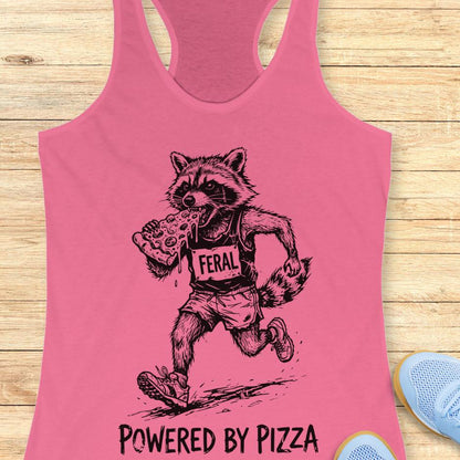 pink tank top with a raccoon runner, with a bib that says - feral, and it is eating a slice of pizza. The tank top has the text  -powered by pizza, and it's on a wooden background