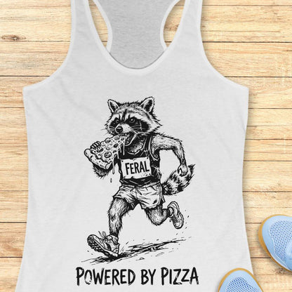 white tank top with a raccoon runner, with a bib that says - feral, and it is eating a slice of pizza. The tank top has the text  -powered by pizza, and it's on a wooden background