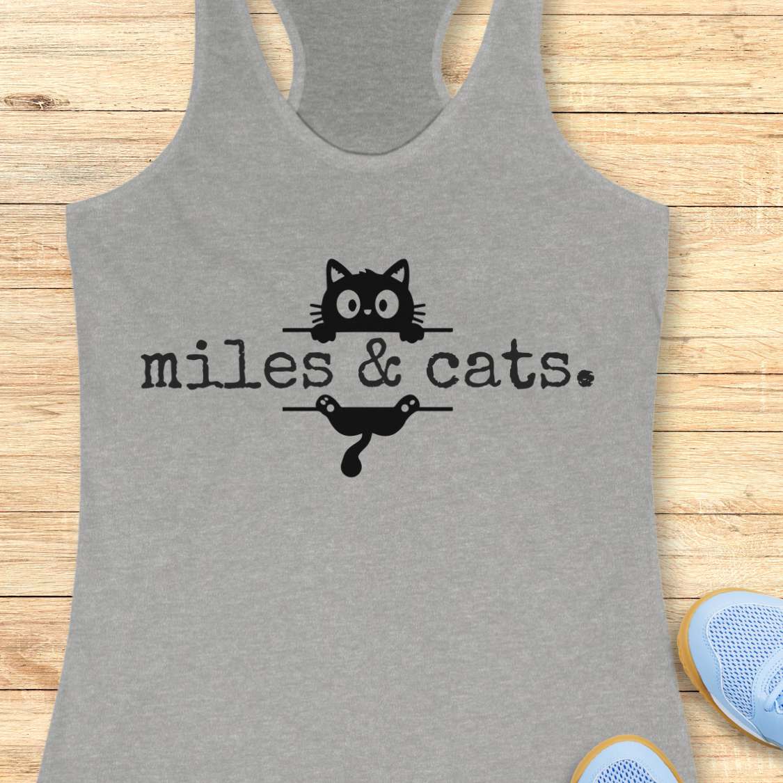 Gray tank top with black text and cat illustrations on a wooden surface