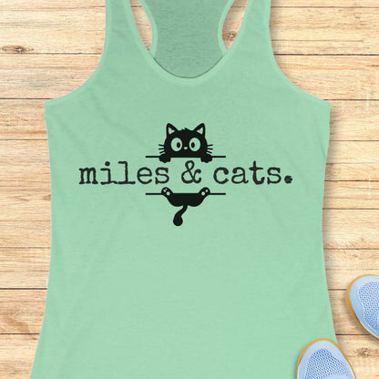 Mint green tank top with 'miles & cats' text and cat illustrations on a wooden surface.