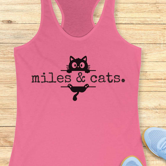 Pink tank top with 'miles & cats' text and cat illustrations on a wooden surface.