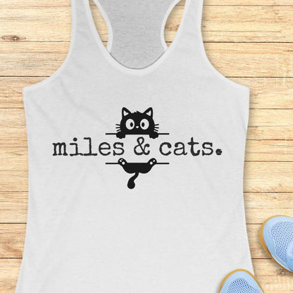 white tank top with 'miles & cats.' text and cat illustrations on a wooden surface.