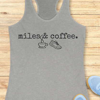 Gray tank top with 'miles & coffee.' text and graphics on a wooden surface.