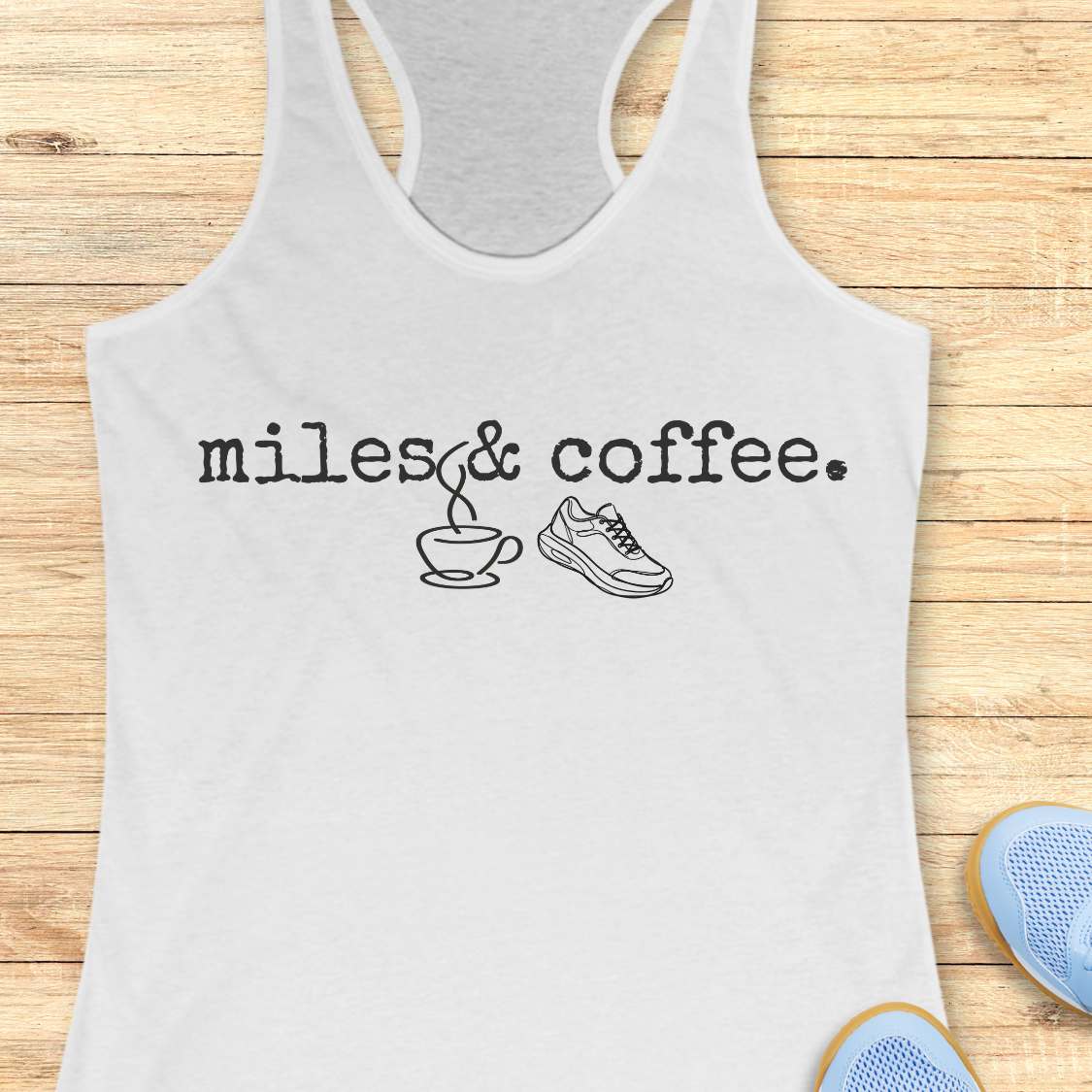 white tank top with 'miles & coffee' text and graphics on a wooden surface