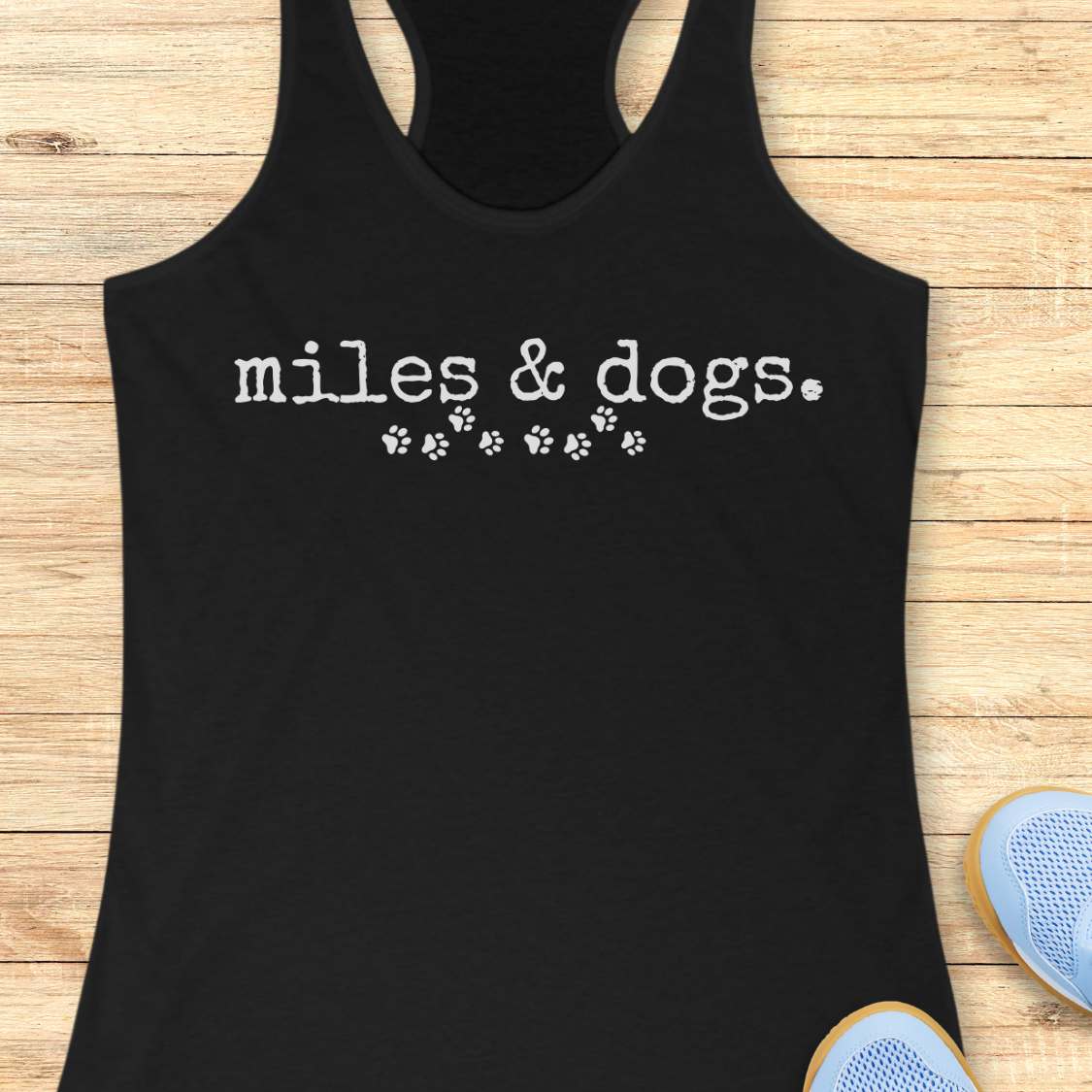 Black tank top with 'miles & dogs' text on a wooden surface