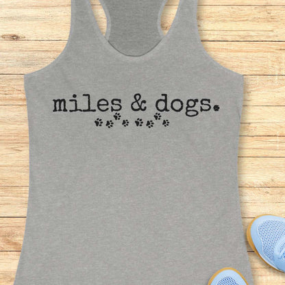 Gray tank top with 'miles & dogs.' text on a wooden surface