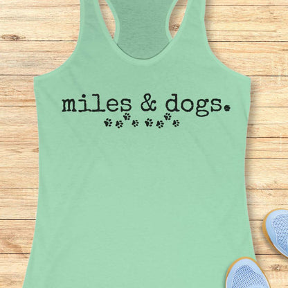 Mint green tank top with 'miles & dogs.' text on a wooden surface